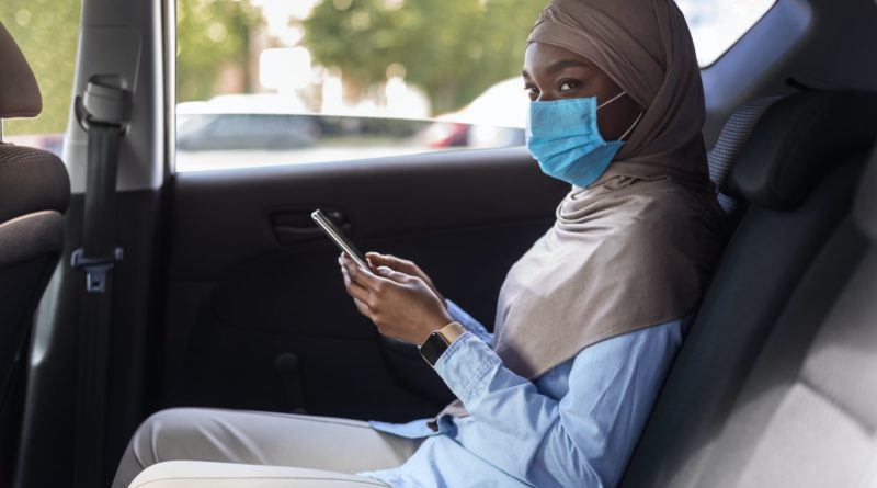 Black muslim businesswoman wearing face mask while using taxi during coronavirus pandemic